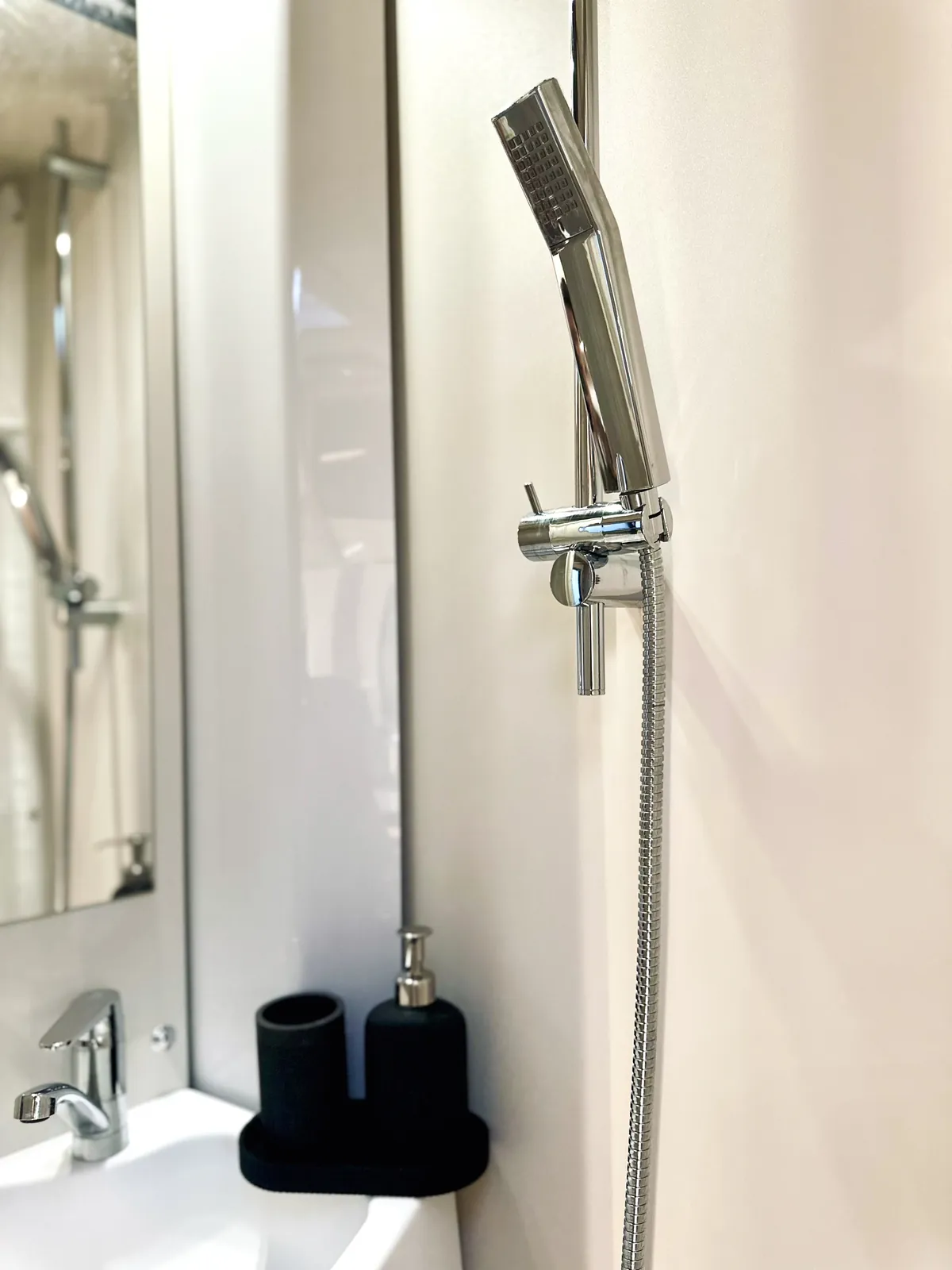 Handbrause auf Gleitstange neben Waschbecken und Spiegel